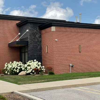 Entrance of Greater Michigan Oral Surgeons & Dental Implant Center in Midland, MI, featuring Boettcher Masonry’s stone and brickwork, side overhang, and prominent front sign under blue skies.