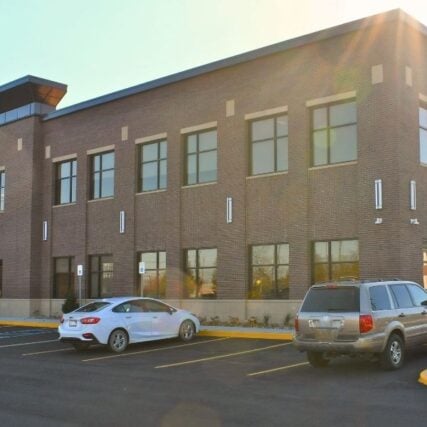 Parking lot of Great Lakes Bay Health Centers Old Town in Saginaw, Michigan, featuring masonry work by Boettcher Masonry with basketweave and running bond brick patterns, blue sign, and clear blue skies.