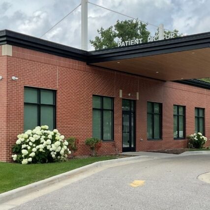 Side view of Greater Michigan Oral Surgeons & Dental Implant Center in Midland, MI, showing Boettcher Masonry’s brickwork with running bond, stack bond, and herringbone patterns, side entrance, and overhang under clear blue skies.