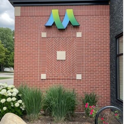 Close-up of Greater Michigan Oral Surgeons & Dental Implant Center in Midland, MI, featuring Boettcher Masonry’s running bond, stack bond, and herringbone brick patterns with logo sign, flowers, and landscaped greenery below.