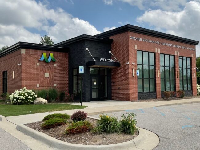 Exterior of Greater Michigan Oral Surgeons & Dental Implant Center in Midland, MI, featuring expert masonry by Boettcher Masonry with running bond, stack bond, and herringbone brick patterns under blue skies.