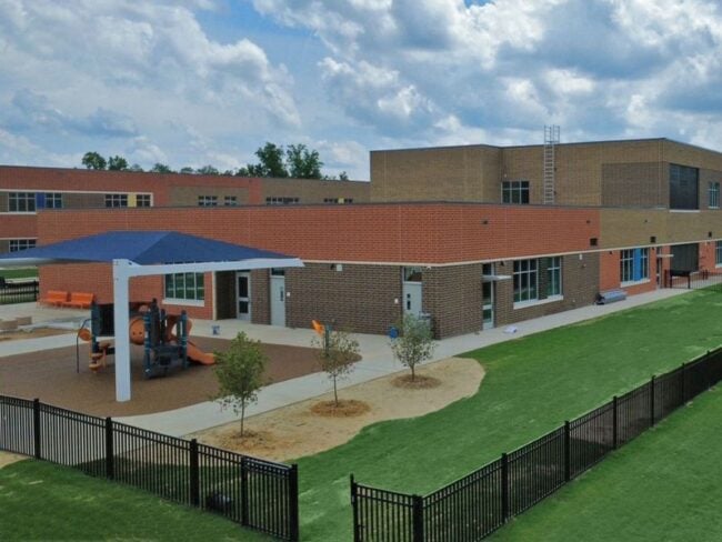 Exterior of E-53 Pleasant Plains Elementary School featuring 320,000 utility bricks, special shapes by Palmetto, and 7,500 colorful glazed bricks from Belden Brick. Playground and fence.