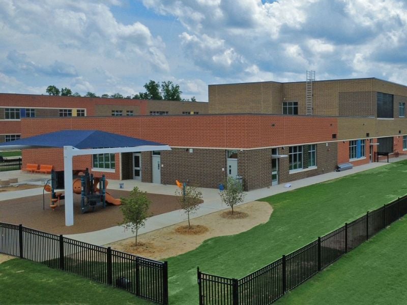 Exterior of E-53 Pleasant Plains Elementary School featuring 320,000 utility bricks, special shapes by Palmetto, and 7,500 colorful glazed bricks from Belden Brick. Playground and fence.