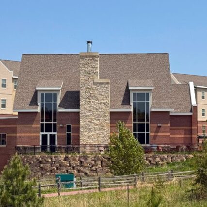 Back view of Northern Michigan University’s Weston Hall featuring Boettcher Masonry’s stone chimney, tall windows, and detailed brickwork surrounded by natural landscaping, tall grass, and trees.