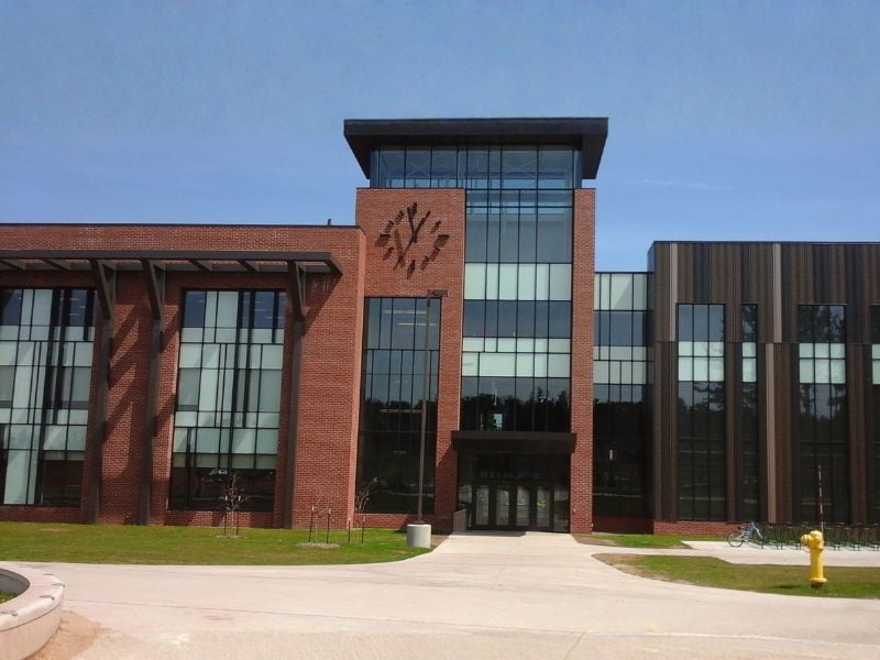 Entrance of Northern Michigan University’s Jamrich Hall featuring Boettcher Masonry’s brickwork, tall glass windows, black architectural accents, and a modern clock on the facade.
