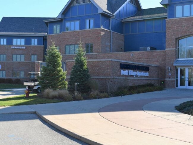 Exterior entrance of Northwood University’s North Village Apartments surrounded by trees, featuring Boettcher Masonry brickwork that blends with the natural wooded setting.