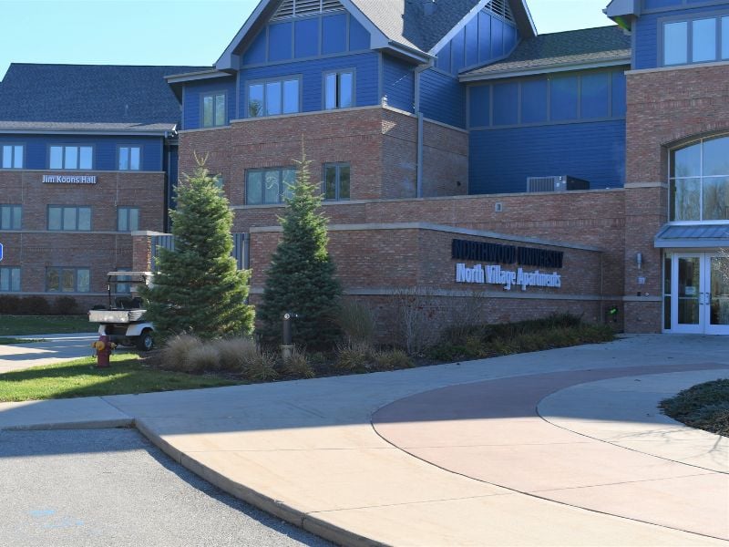 Exterior entrance of Northwood University’s North Village Apartments surrounded by trees, featuring Boettcher Masonry brickwork that blends with the natural wooded setting.
